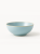 A round ceramic bowl with a smooth matte finish in light blue features a subtle, natural-toned rim.
