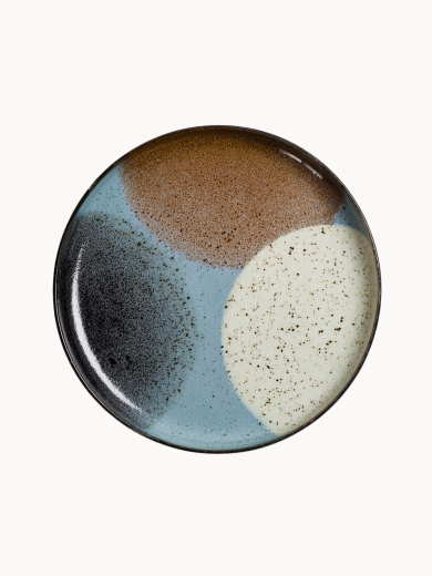 A top-down view on a large ceramic plate with a black rim features an abstract design of color blocks in brown, beige, light blue, and black.