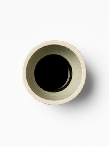 A top-down view on a pedestal ceramic bowl in a light cream color with a subtle crackle glaze and three horizontal black stripes around its middle.
