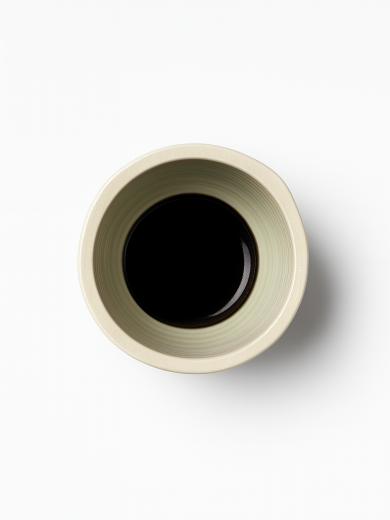 A top-down view on a pedestal ceramic bowl in a light cream color with a subtle crackle glaze and three horizontal black stripes around its middle.