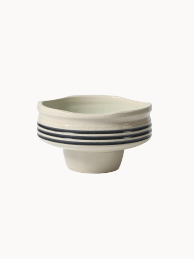 A pedestal ceramic bowl in a light cream color with a subtle crackle glaze and three horizontal black stripes around its middle.