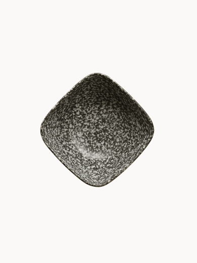 A top-down view on a ceramic bowl with a speckled black and white texture with subtle horizontal ribbed lines, on a plain white background. The deep bowl has a unique, square-like curved rim.